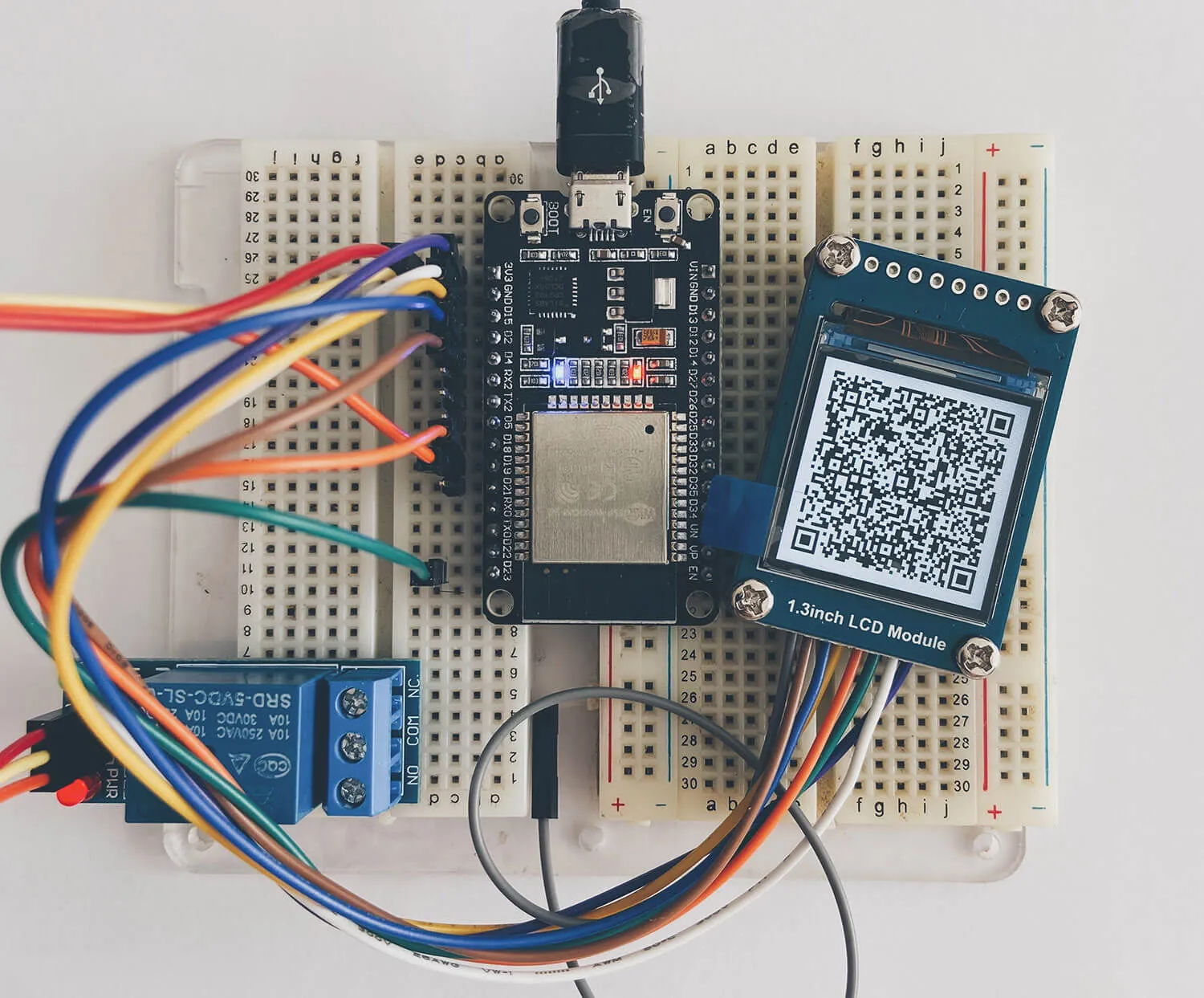 Breadboard prototype with an ESP32, a relay and a screen showing a QR code